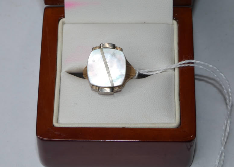 A ring with a rectangular, reflective stone set in a metal band, displayed in an open wooden box with a white interior.